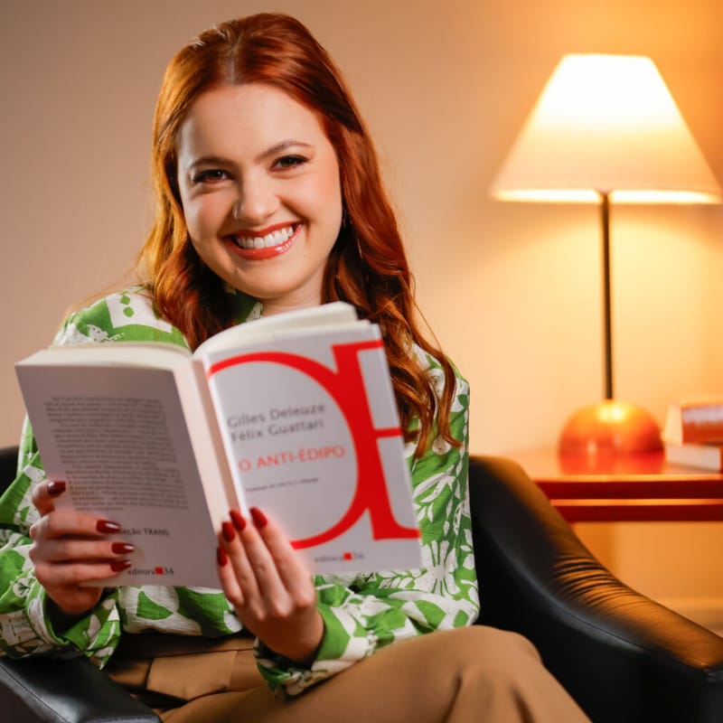 Blanka Finoketti, psicóloga, sorrindo sentada em uma poltrona com um livro aberto nas mãos